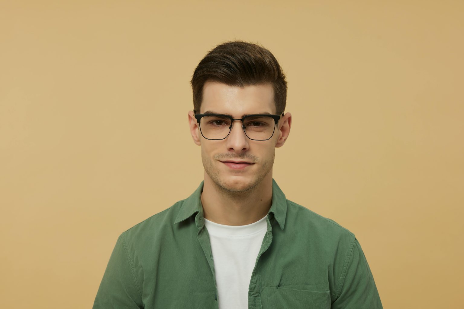 Close-up portrait of a fashionable young man wearing glasses and a green shirt against a beige background.